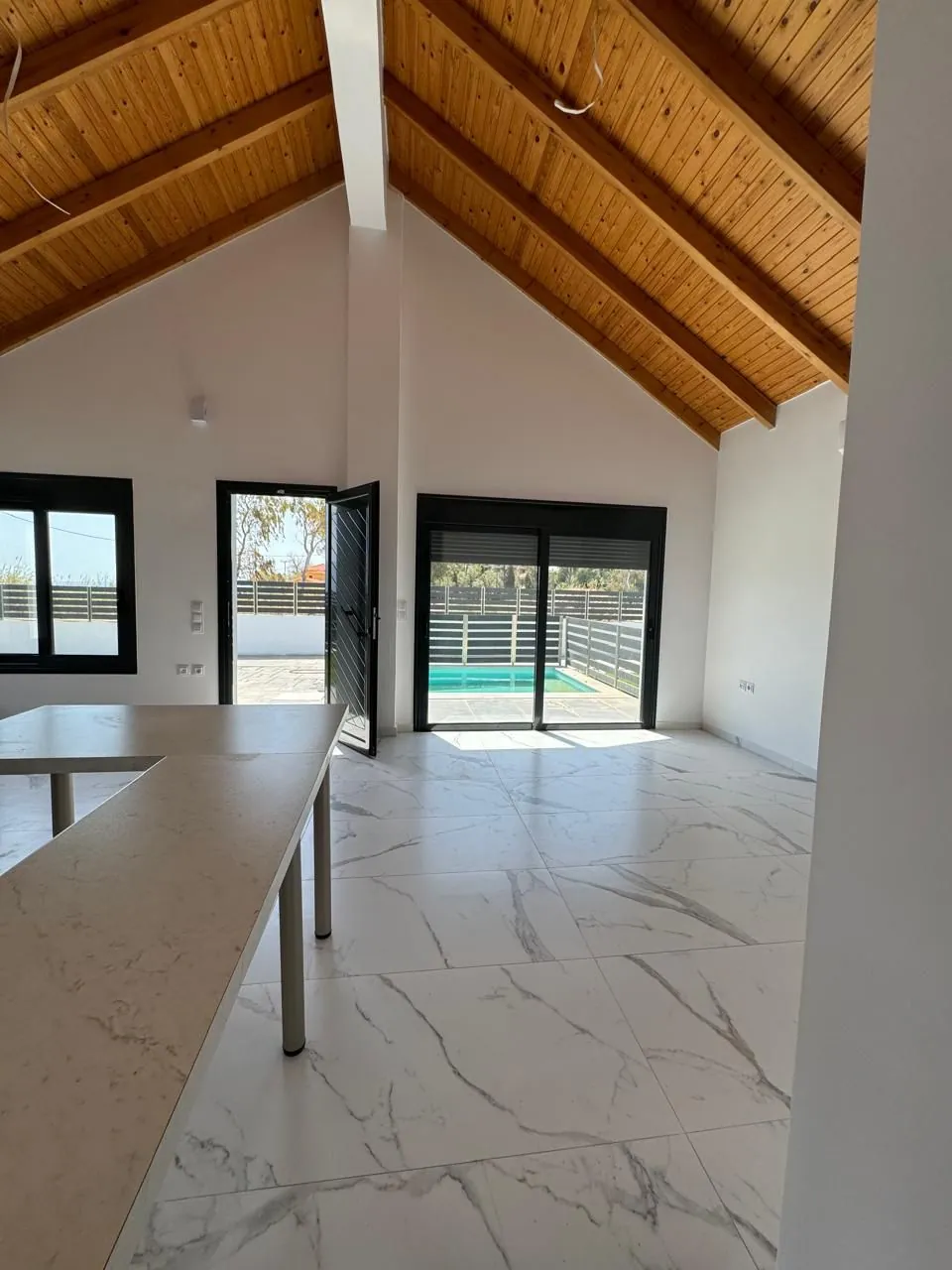 Double-height living room with exposed timber roof frame and marble-effect floor tiling